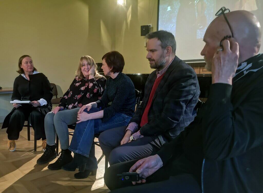 Uczestnicy debaty siedzą w rzędzie w sali Akademii Sztuki w Szczecinie, w tle ekran prezentacji