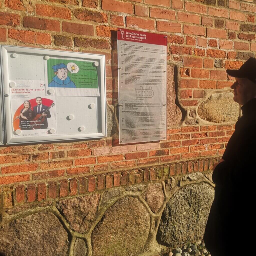 Plakat wydarzenia w gablocie na ceglanym murze kościoła św. Piotra w Wolgaście